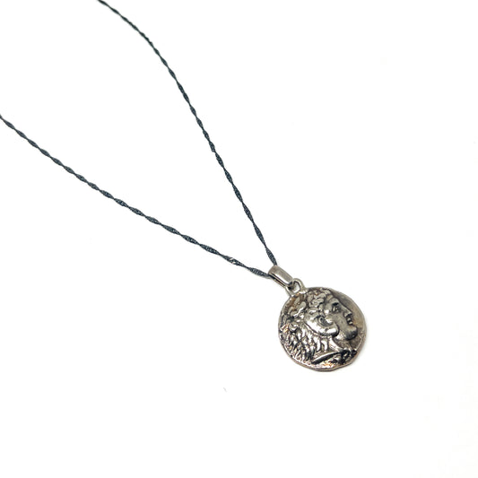 A delicate necklace with a dark, twisted chain and a round silver pendant featuring a detailed profile of Alexander the Great.