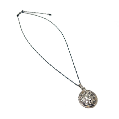 A necklace with a fine, dark chain and a round silver pendant featuring a detailed profile of Alexander the Great.