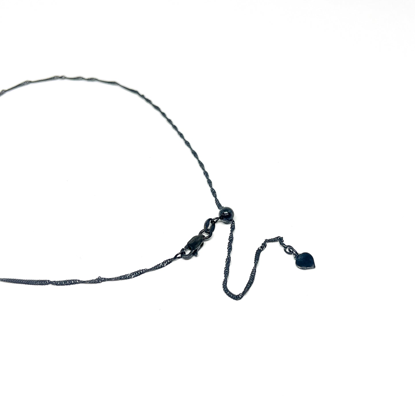 Close-up of the clasp and adjustable chain of a delicate dark necklace with a small heart-shaped charm at the end.