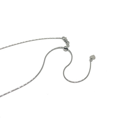 Close-up of a delicate silver necklace with an adjustable diamond-cut snake chain and a small heart charm at the end.