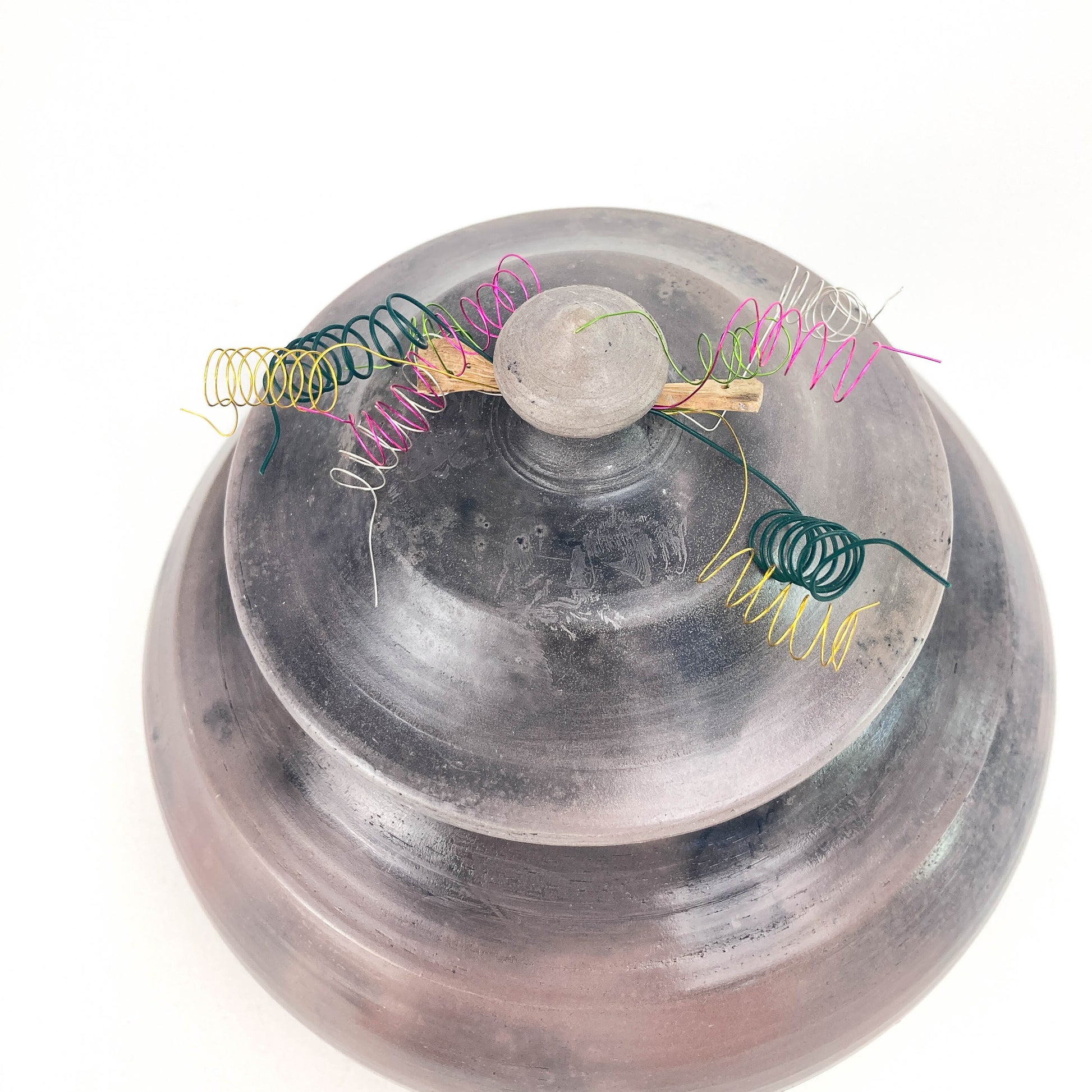 A textured, lidded jar features a coil spring lid adorned with colorful, delicate wire spirals and a central stone knob.