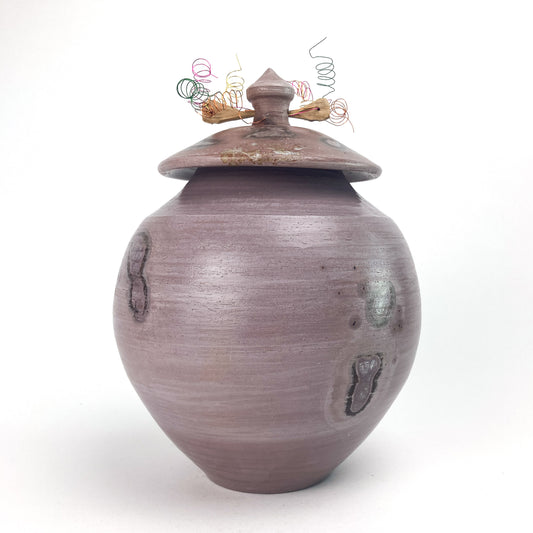 A lavender, textured ceramic jar with a fitted lid and coiled wire decoration.