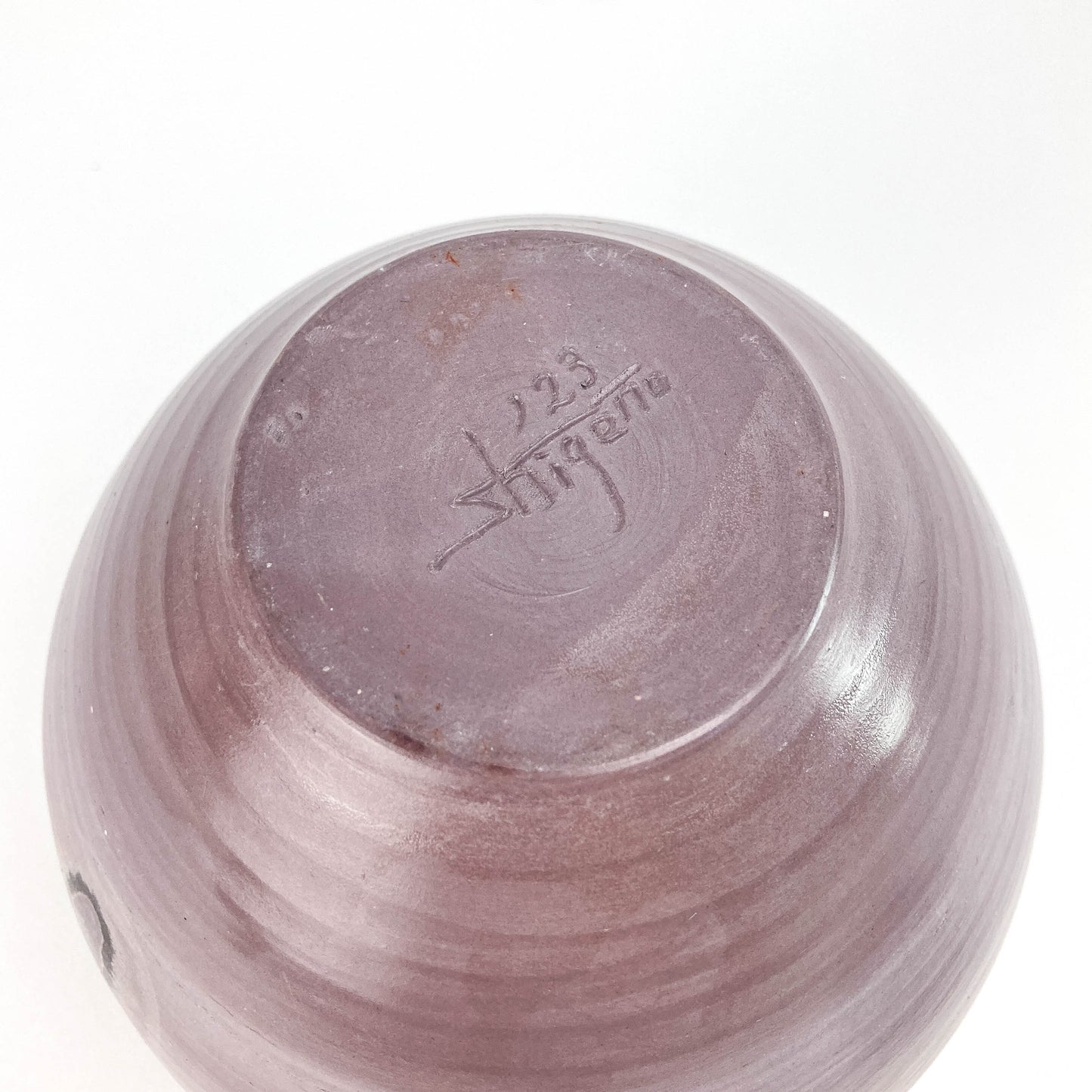 Close-up of a textured ceramic jar with the numbers '123' and the word 'shigeno' inscribed on its surface.