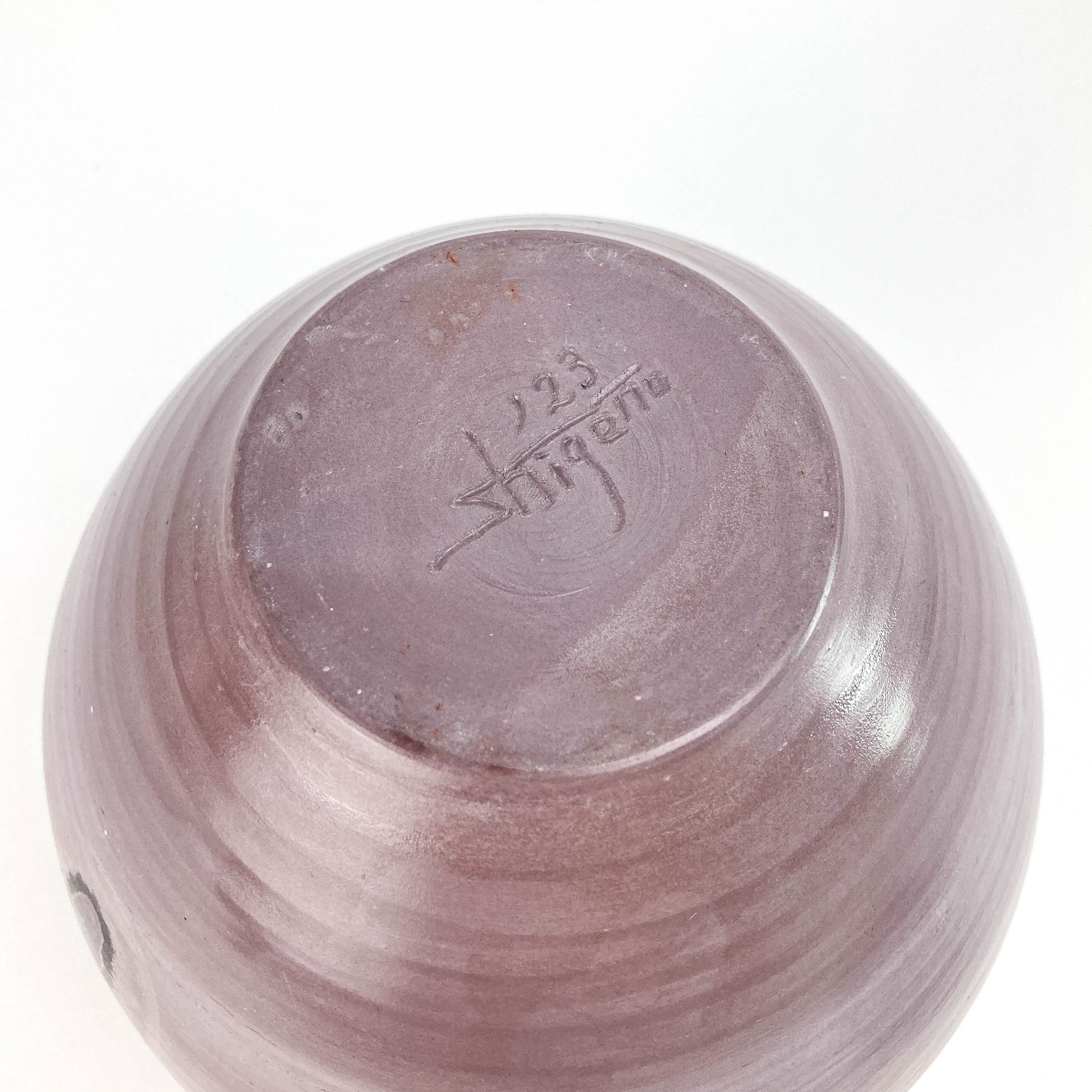Close-up of a textured ceramic jar with the numbers '123' and the word 'shigeno' inscribed on its surface.
