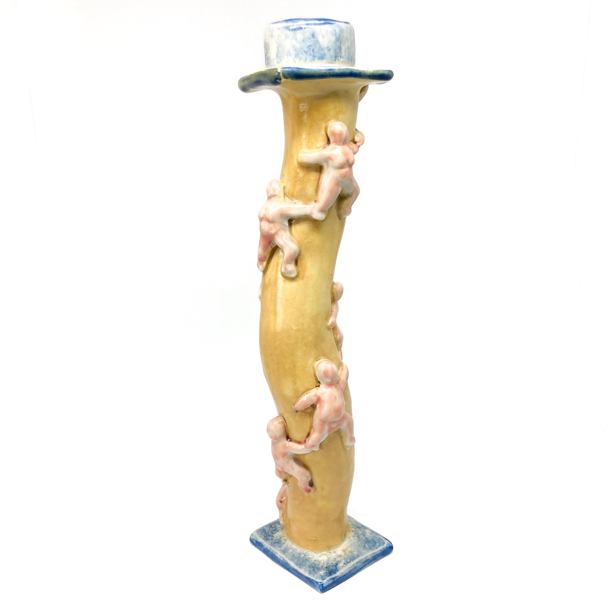 A yellow ceramic candlestick with a wavy stem features small, light-colored figures climbing upwards. The base and top have blue and white details.