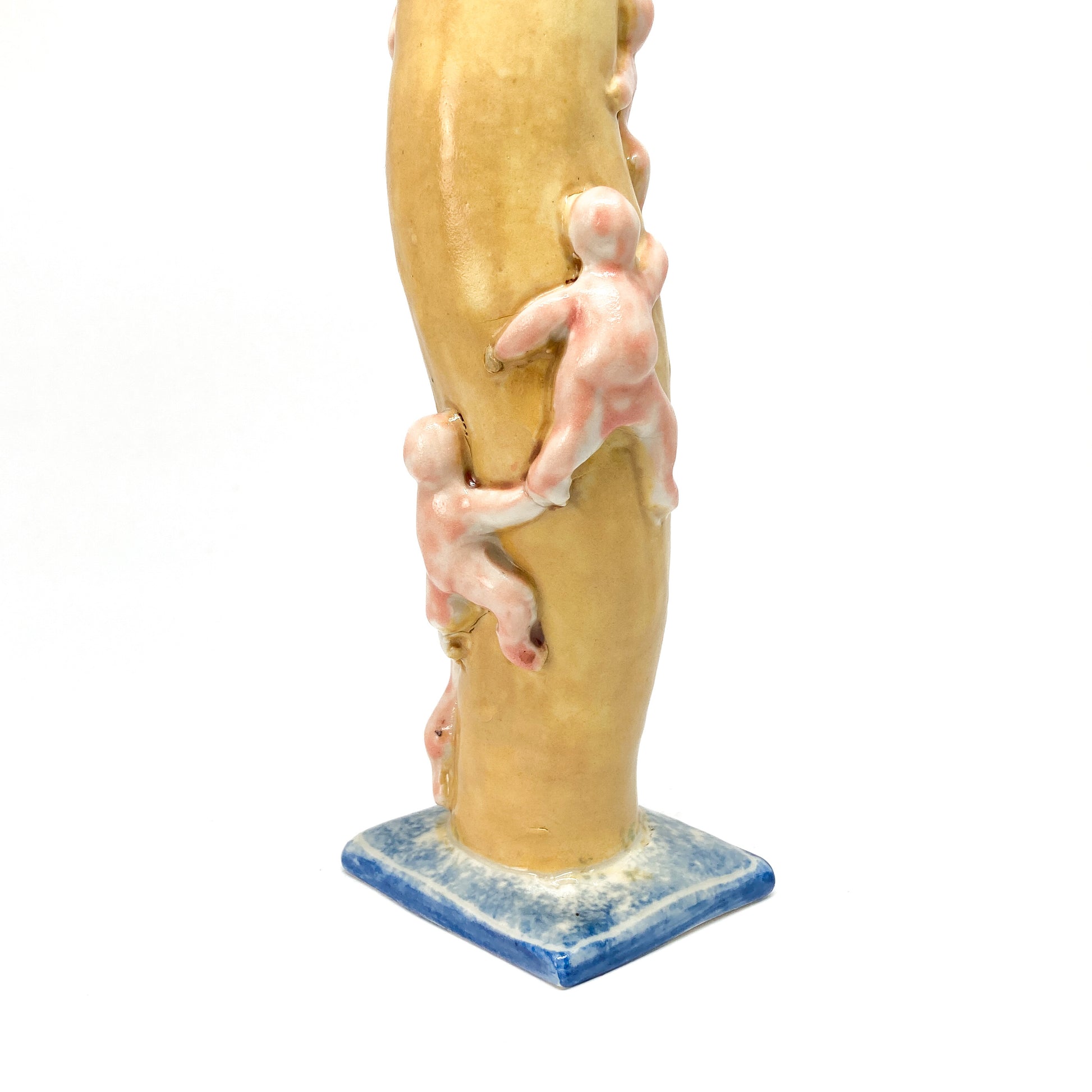 Close-up of a yellow ceramic candlestick stem with small, light-colored figures appearing to climb it. The base has blue and white details.