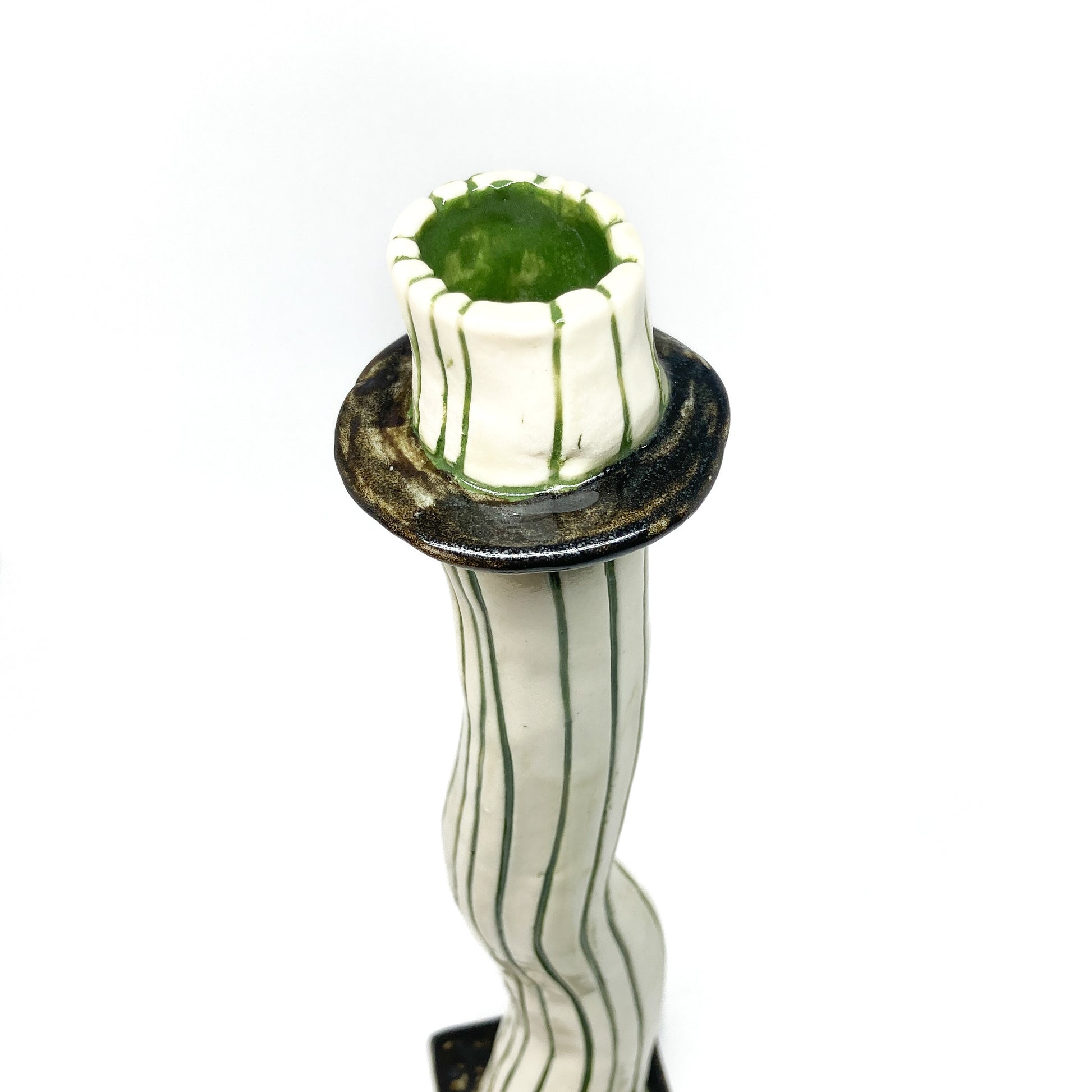 The top of a white ceramic candlestick with dark green vertical stripes and a wavy form features a dark green rim and interior.