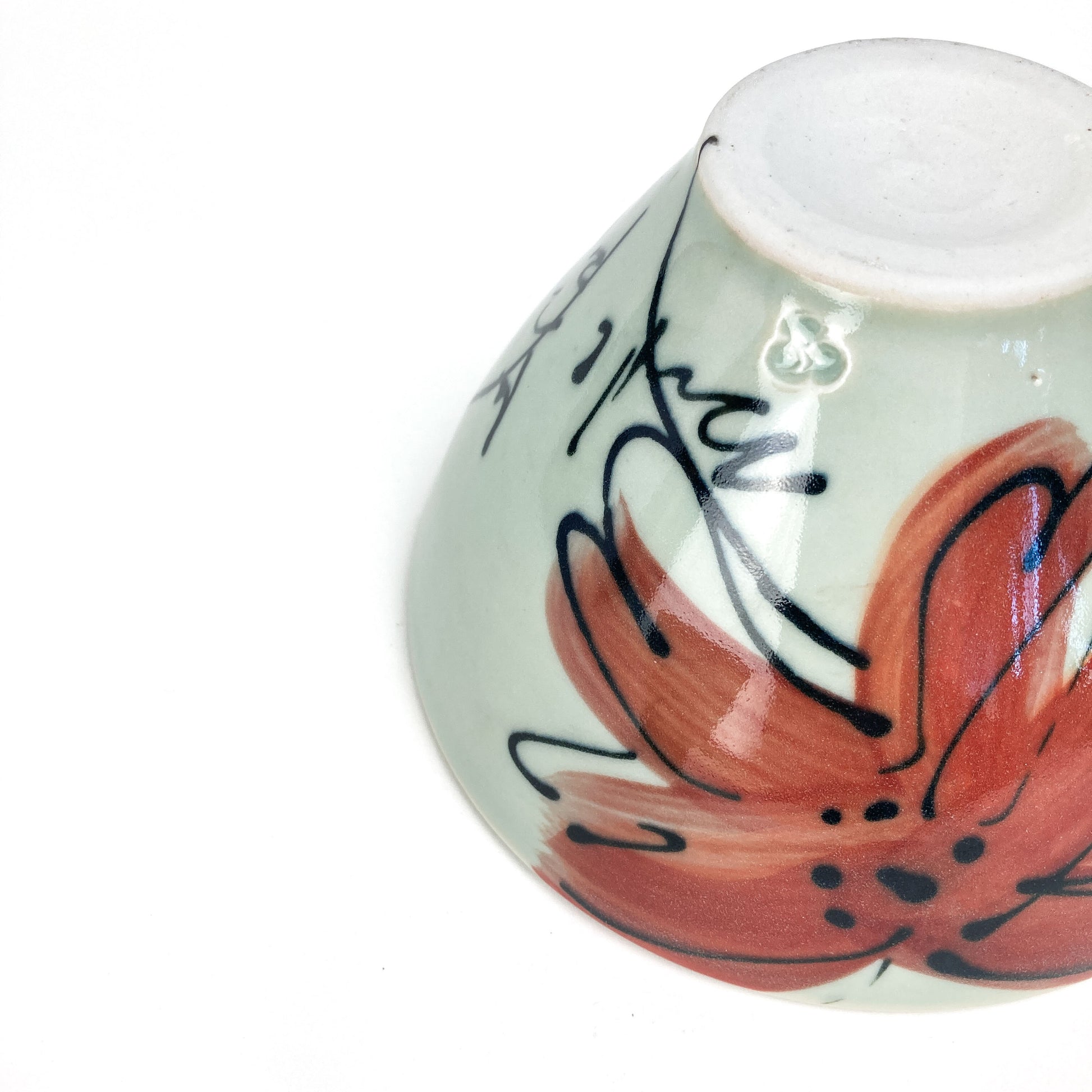 A ceramic bowl, angled view, showing a hand-painted floral design on its side. The bowl has a smooth, glazed finish and a flat base.