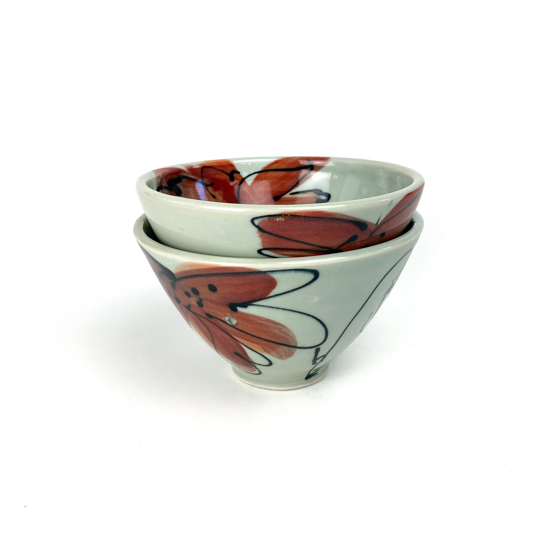 Two small, conical ceramic bowls stacked on top of each other. Each bowl has a hand-painted floral design on its side and a smooth, glazed finish.