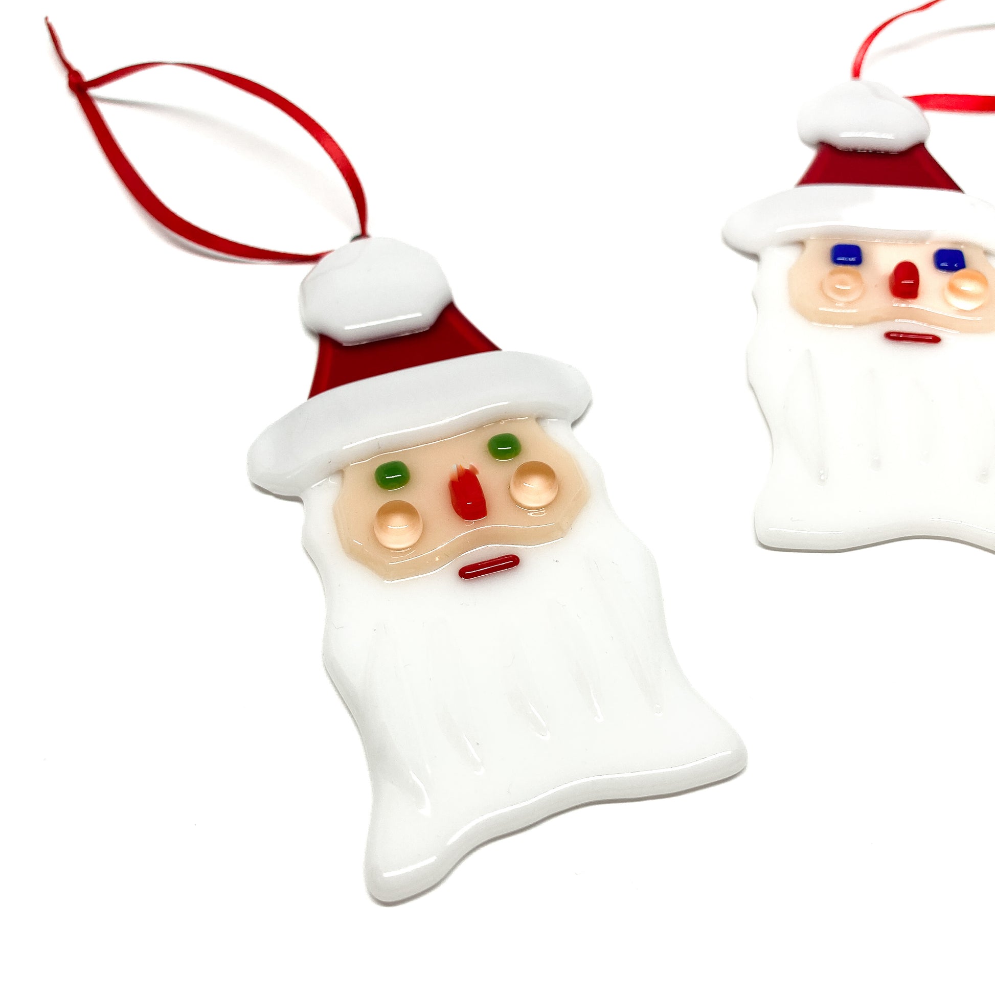 Close-up of a glass Santa ornament with a red ribbon, viewed from above, with another Santa ornament partially visible.