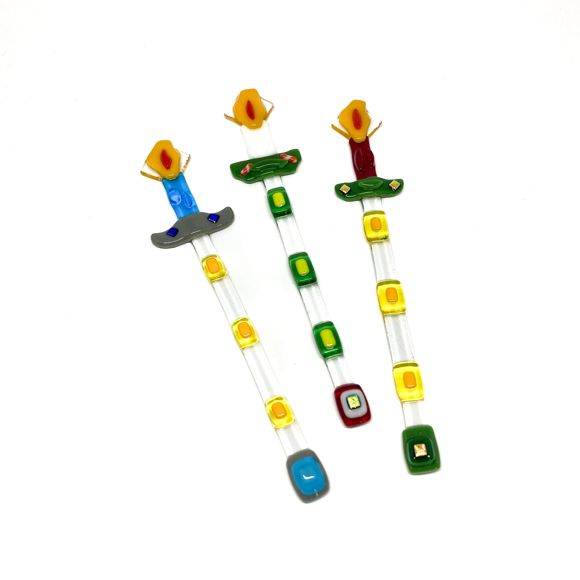 Three glass stir sticks shaped like candles, decorated with colorful glass pieces.