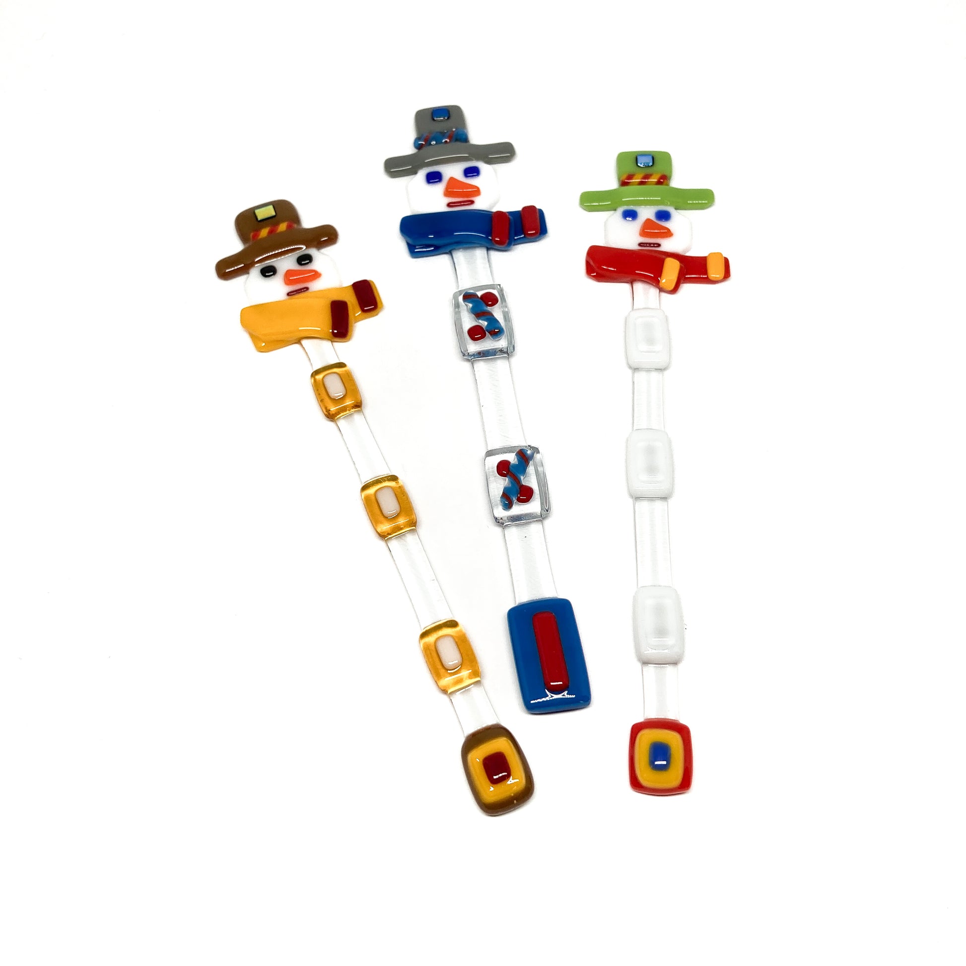 Three glass stir sticks shaped like snowmen, decorated with colorful glass pieces.