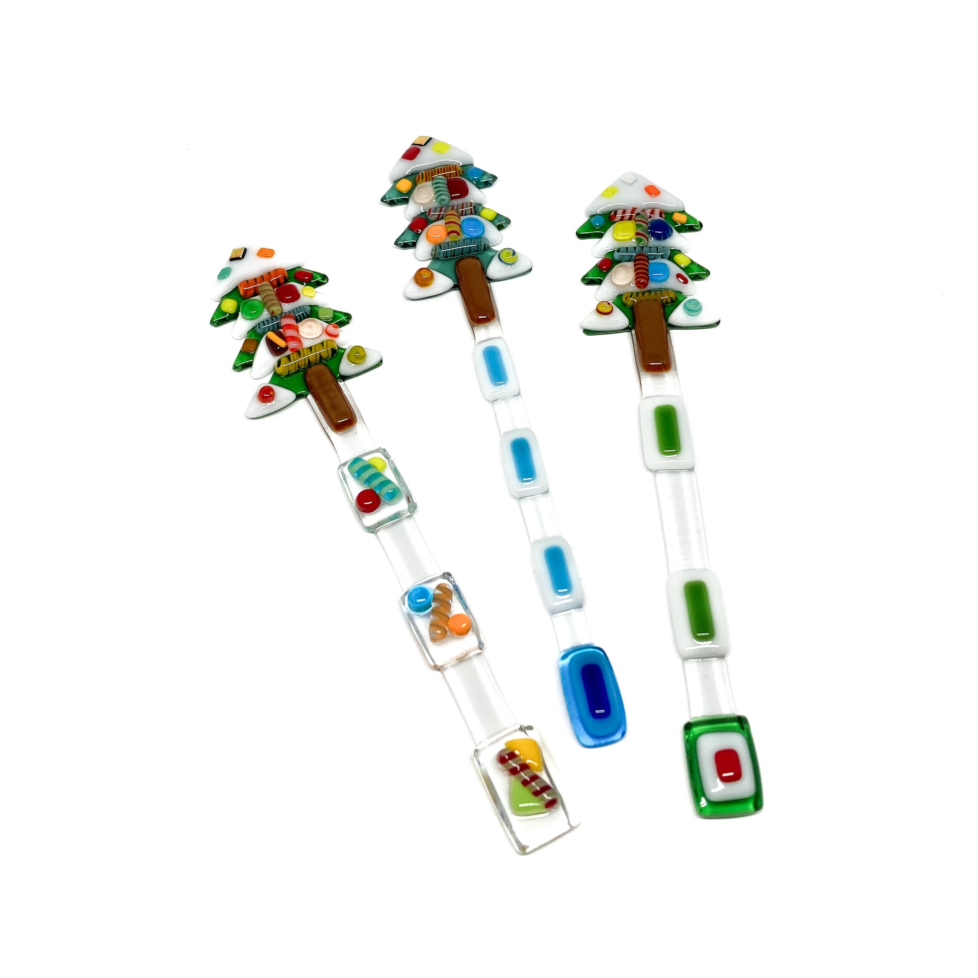 Three glass stir sticks shaped like Christmas trees, decorated with colorful glass pieces.