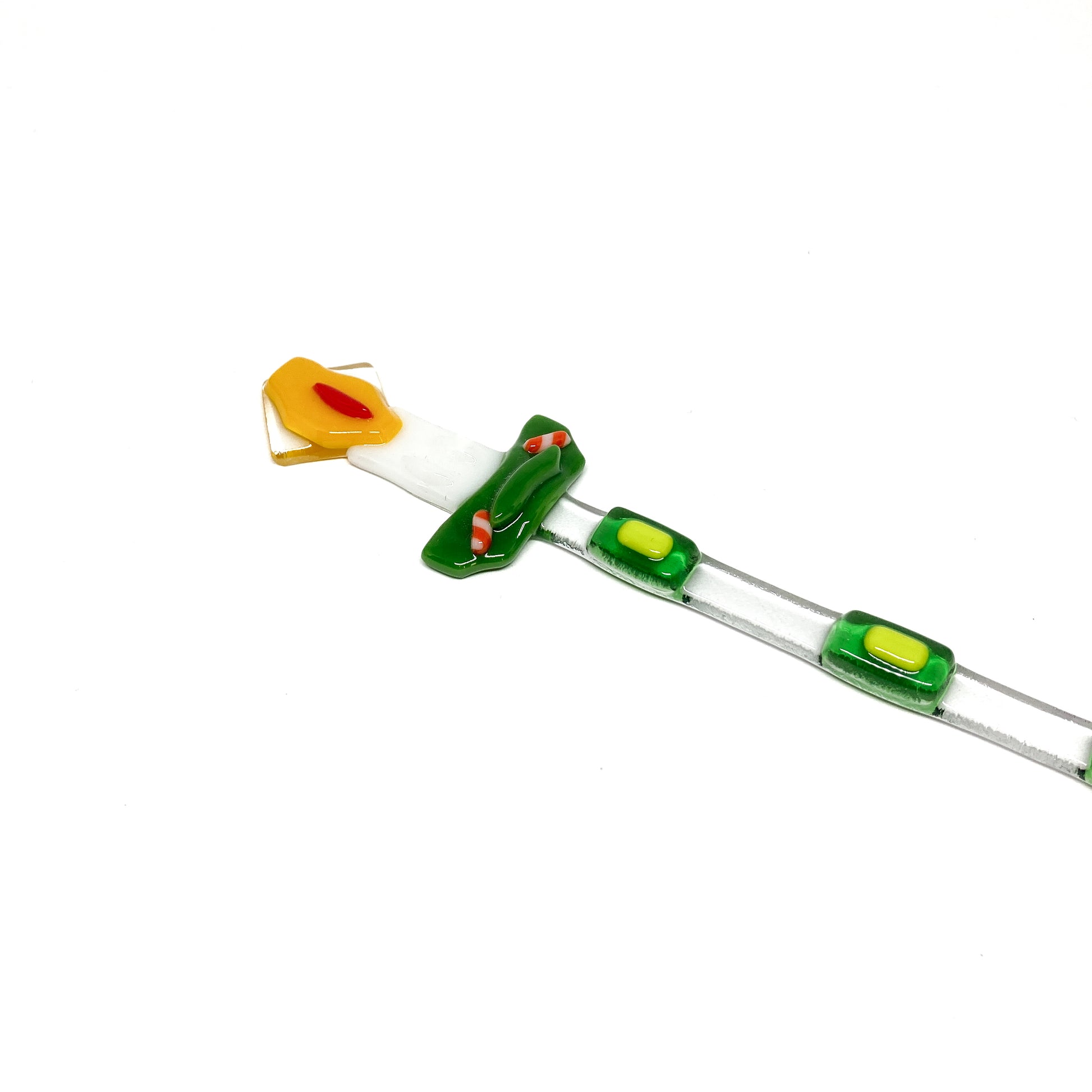 A glass stir stick shaped like a candle, decorated with colorful glass pieces.