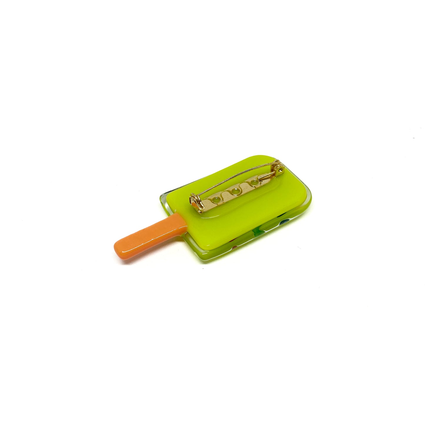 Back view of a green glass pin shaped like a popsicle with an orange stick and a gold pin backing.