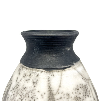 Close-up of the textured black neck and rim of a ceramic vase with a crackled white and black body.