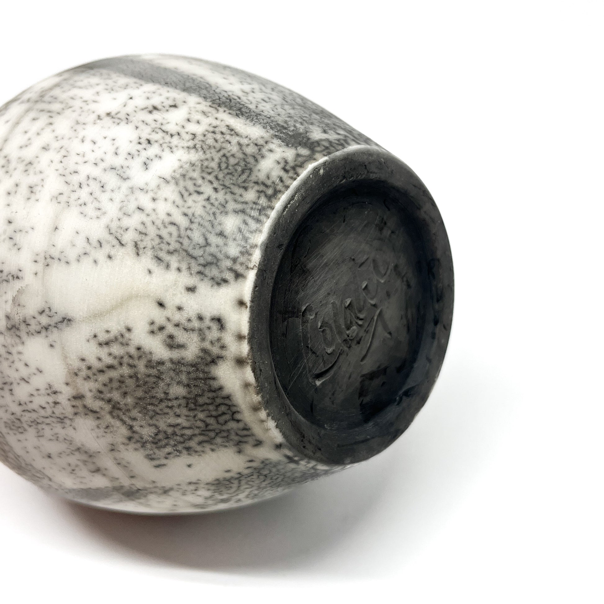 Bottom view of a ceramic vase with a crackled black and white glaze and a black base with inscribed text.