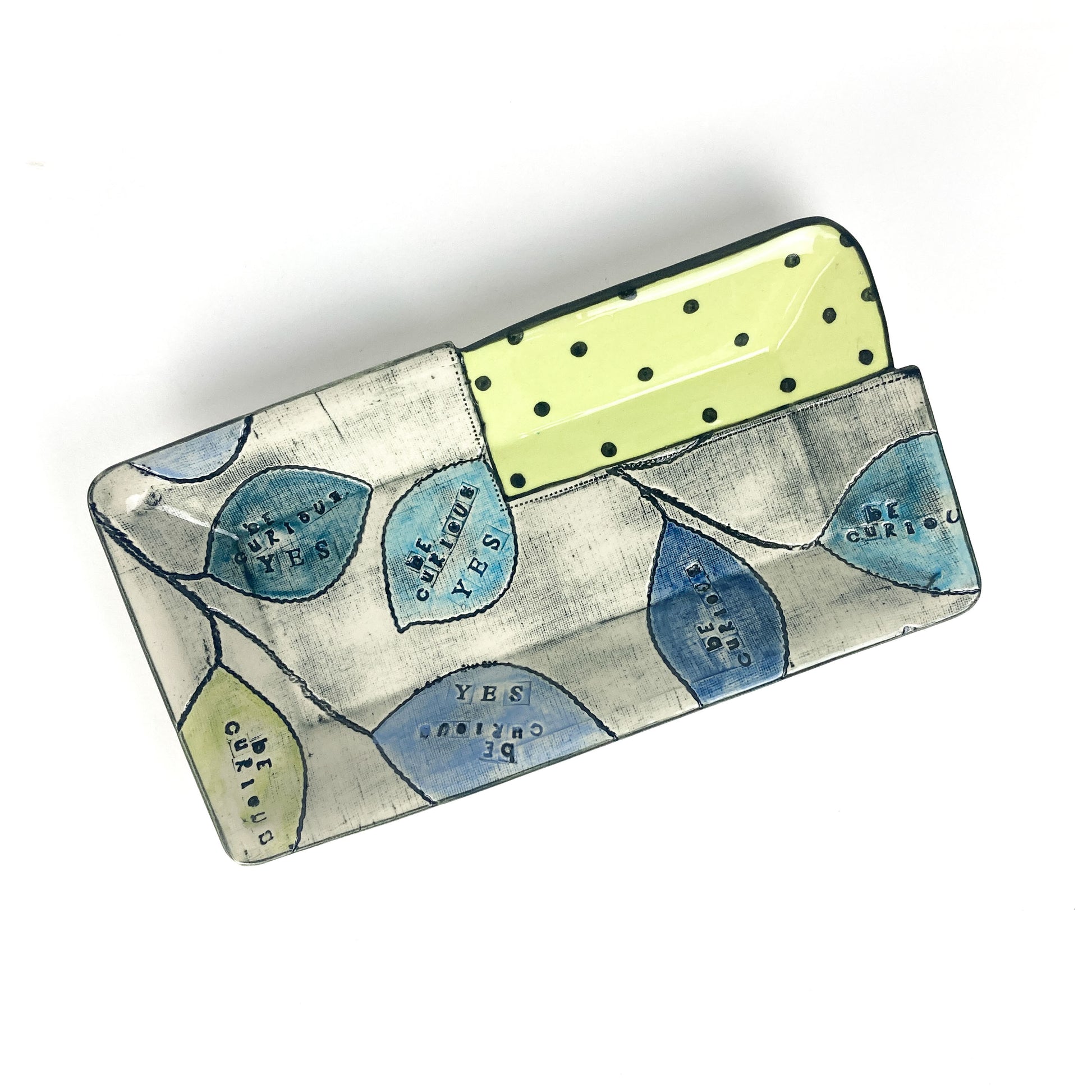 Rectangular ceramic platter with leaf patterns and a dotted section reading “Be Curious” and “Yes”.