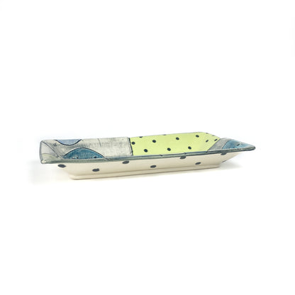 Underside of the rectangular ceramic platter featuring polka dots and the maker’s signature stamp.