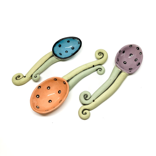 Set of three funky spoons with polka-dot bowls and whimsical curled handles in a playful design.