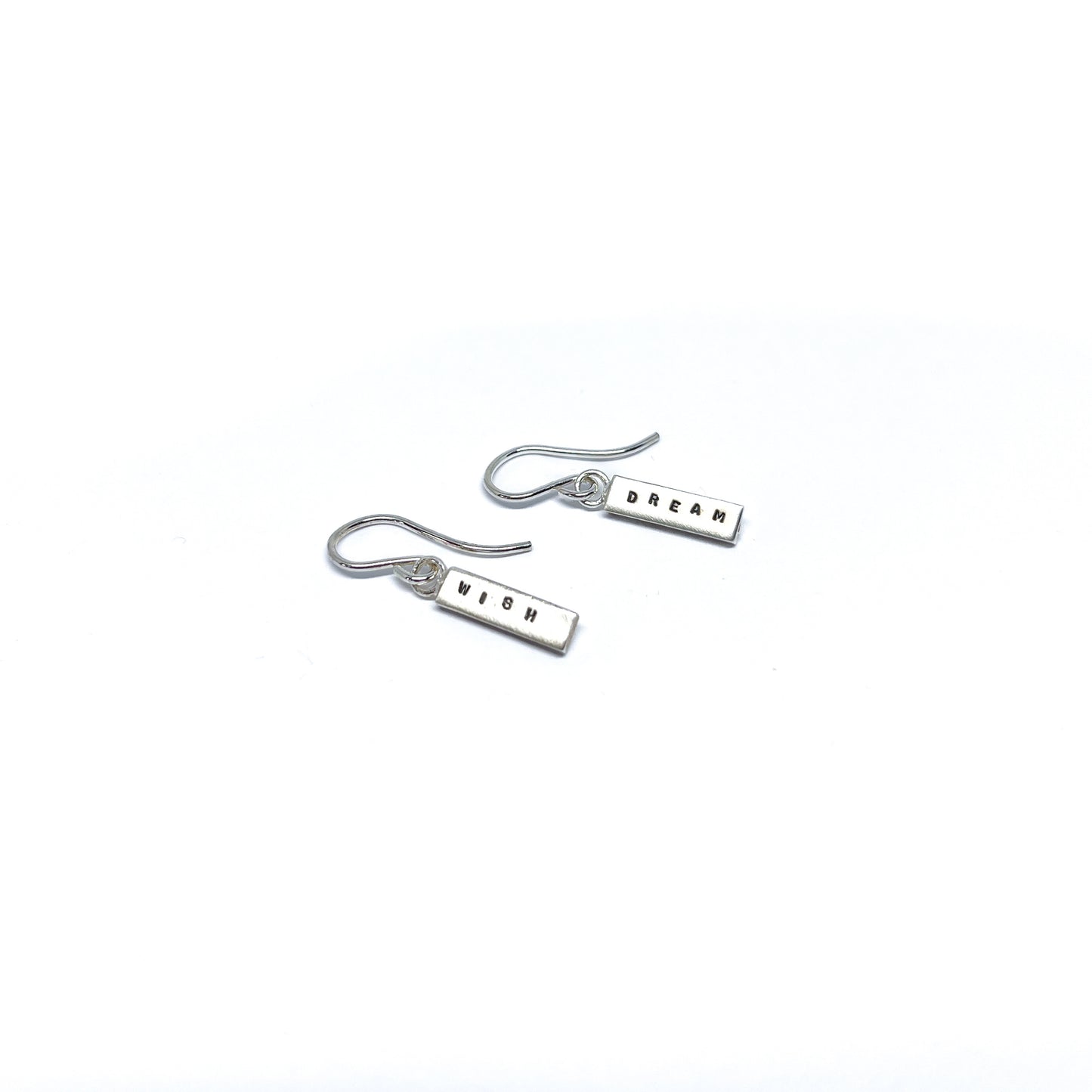 Two silver earrings with rectangular charms, one reads "DREAM" and the other "WISH".
