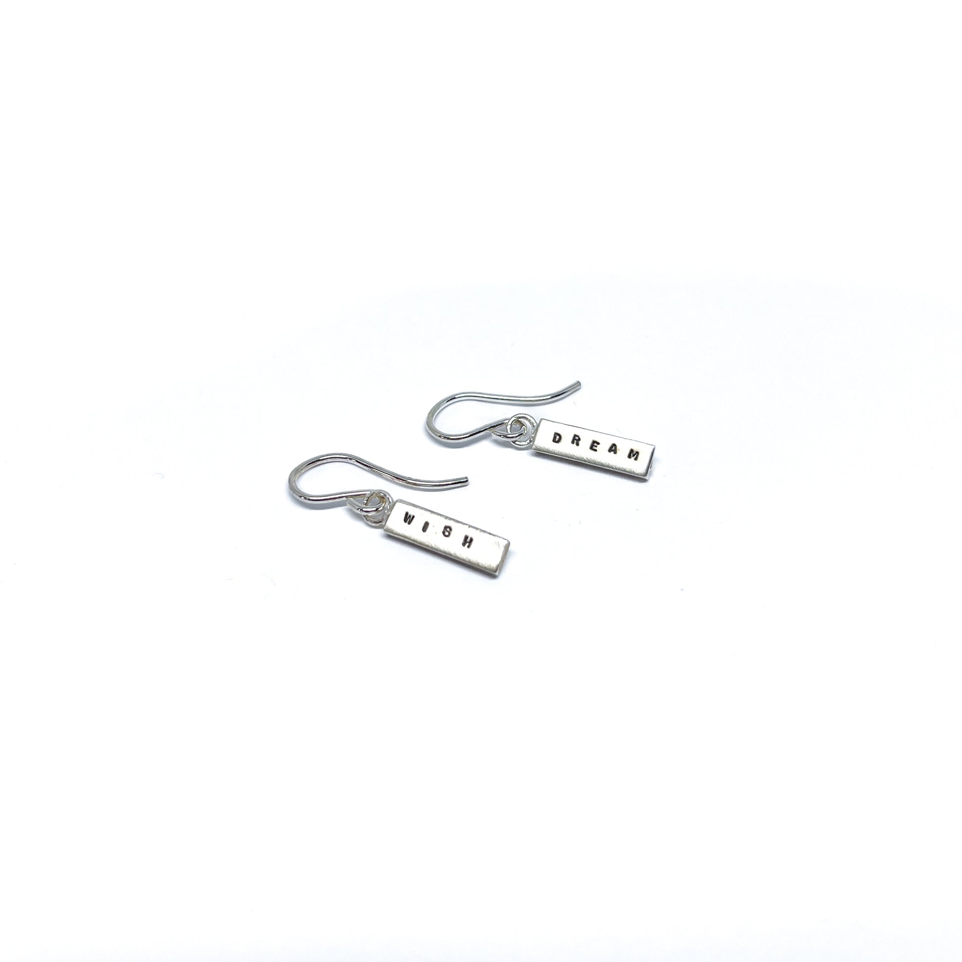 Two silver earrings with rectangular charms, one reads "DREAM" and the other "WISH".