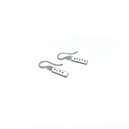 Two silver earrings with rectangular charms, one reads "DREAM" and the other "WISH".