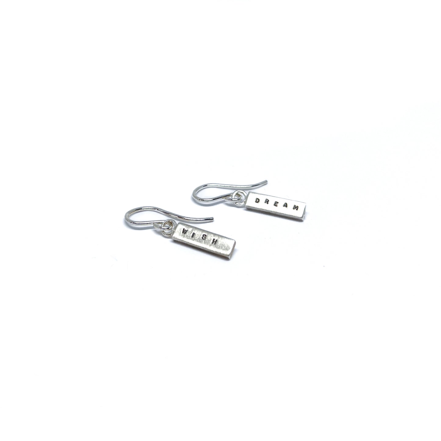 Two silver earrings with rectangular charms, one reads "DREAM" and the other "WISH".