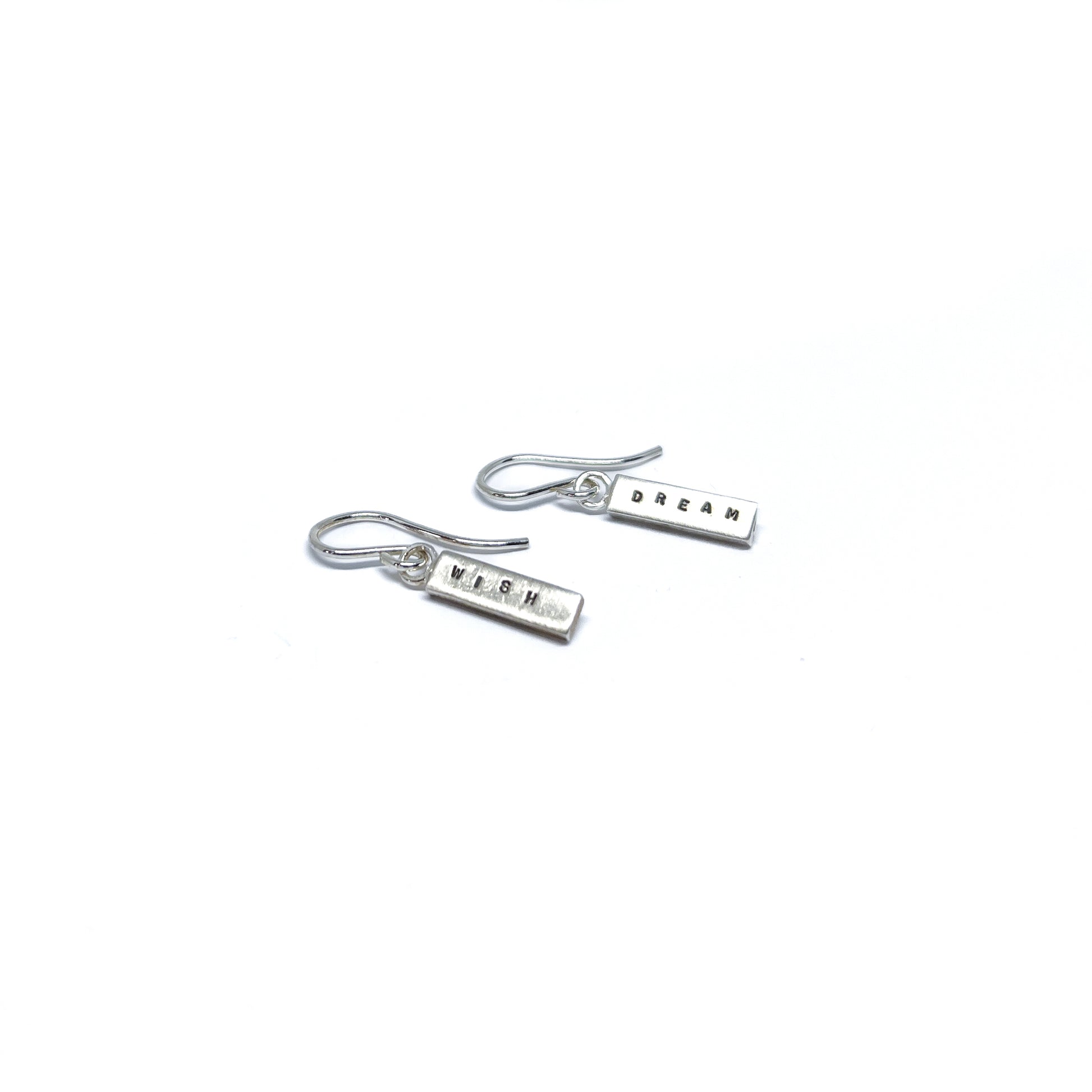 Two silver earrings with rectangular charms, one reads "DREAM" and the other "WISH".