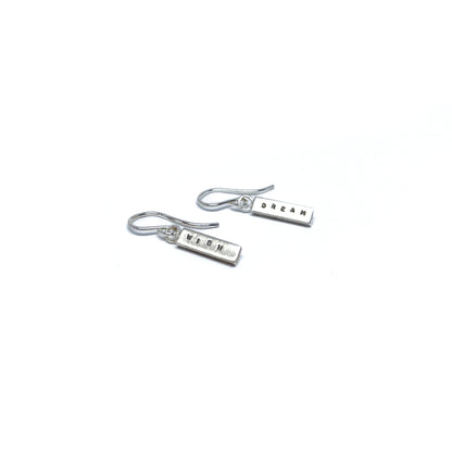 Two silver earrings with rectangular charms, one reads "DREAM" and the other "WISH".
