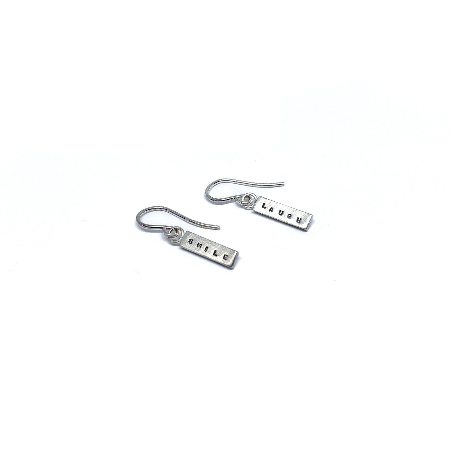 Two silver earrings with rectangular charms, one reads "SMILE" and the other "LAUGH".