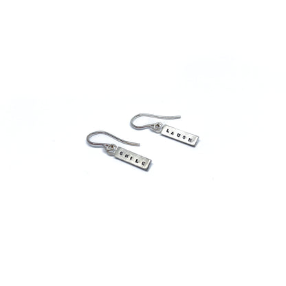 Two silver earrings with rectangular charms, one reads "SMILE" and the other "LAUGH".