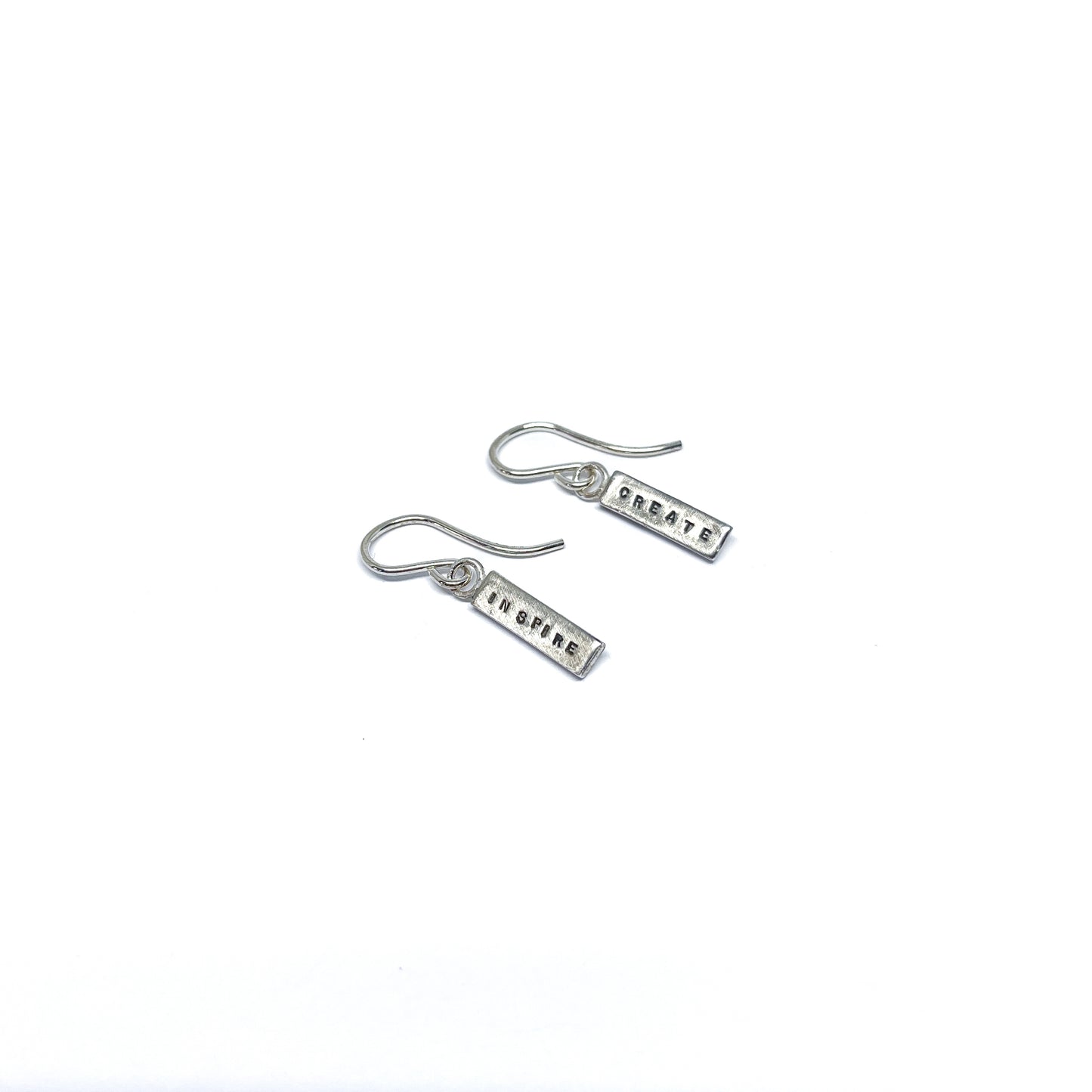 Two silver earrings with rectangular charms, one reads "CREATE" and the other "INSPIRE".