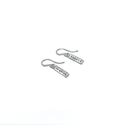 Two silver earrings with rectangular charms, one reads "CREATE" and the other "INSPIRE".