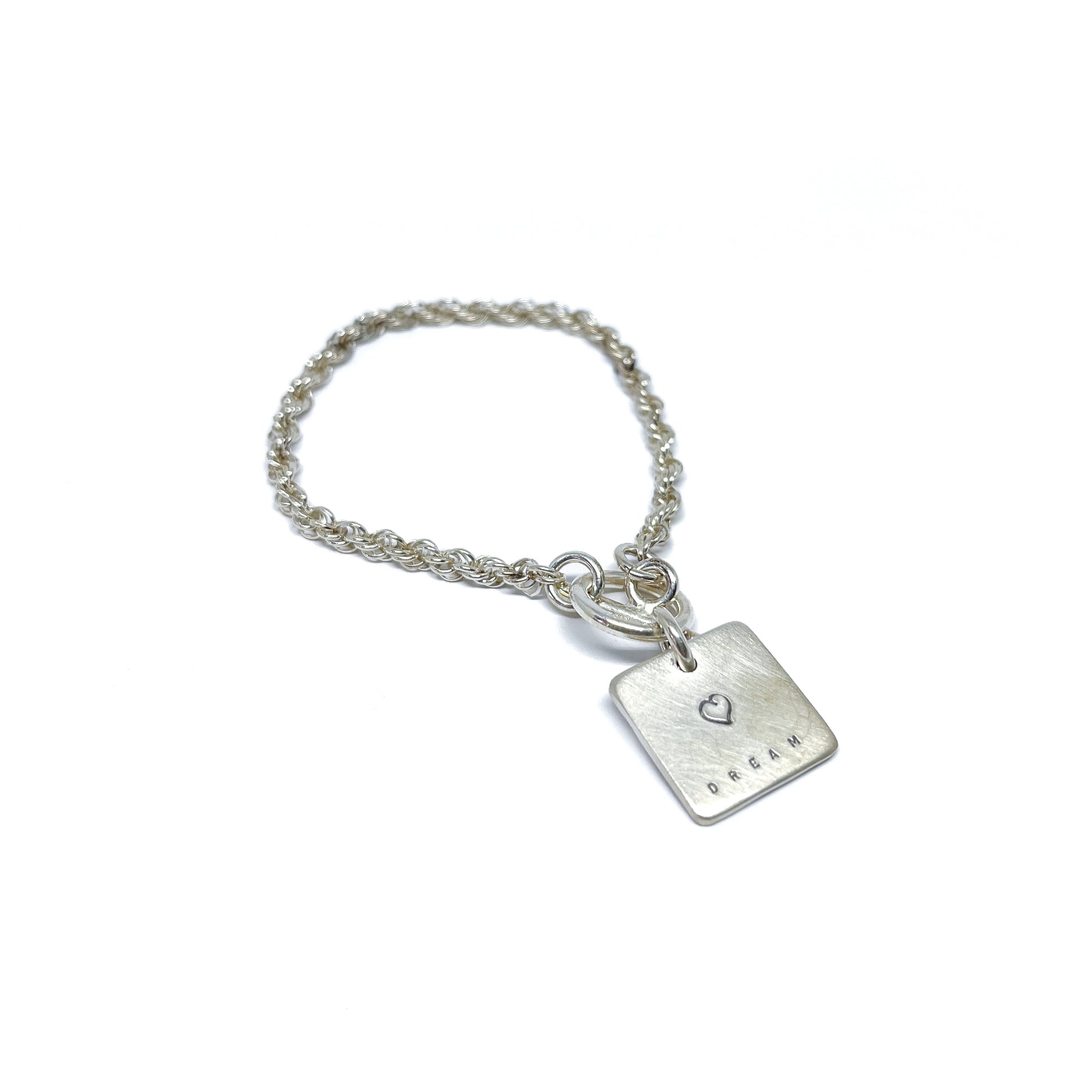 Silver bracelet with a square charm with a heart and the word "DREAM" engraved on it.