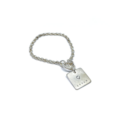 Silver bracelet with a square charm with a heart and the word "DREAM" engraved on it.
