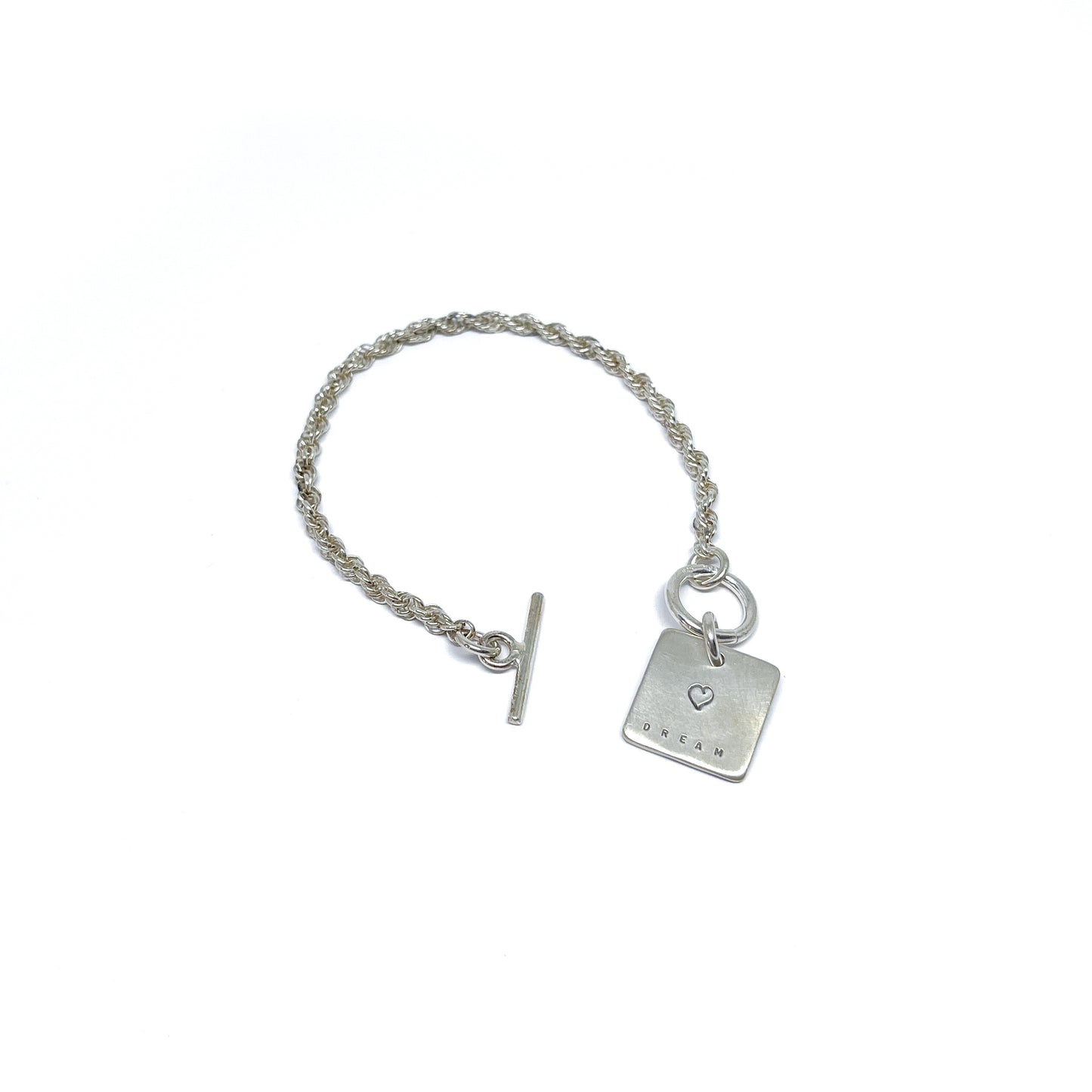 Silver bracelet with a square charm with a heart and "DREAM" engraved on it, with a t-bar clasp.