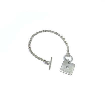 Silver bracelet with a square charm with a heart and "DREAM" engraved on it, with a t-bar clasp.