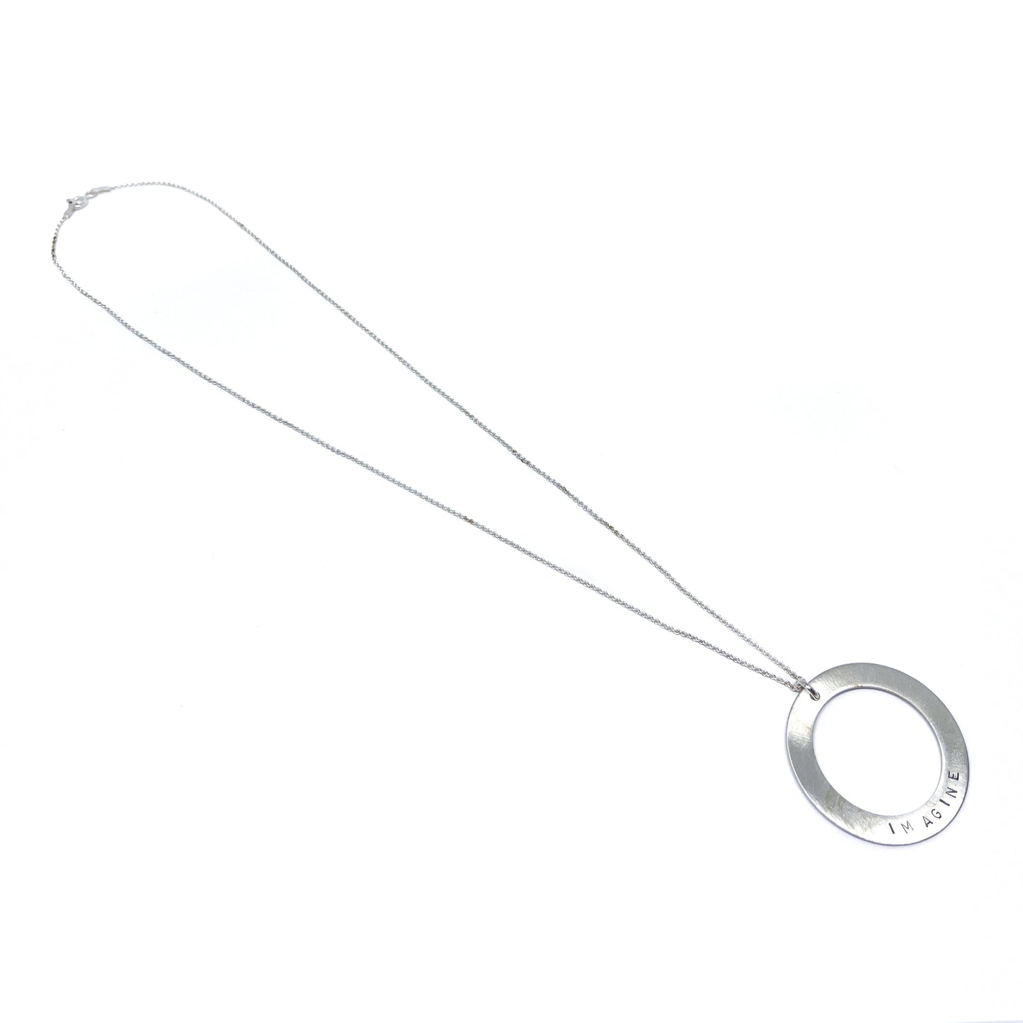 Silver necklace with a circular pendant engraved with the word "IMAGINE," lying flat.