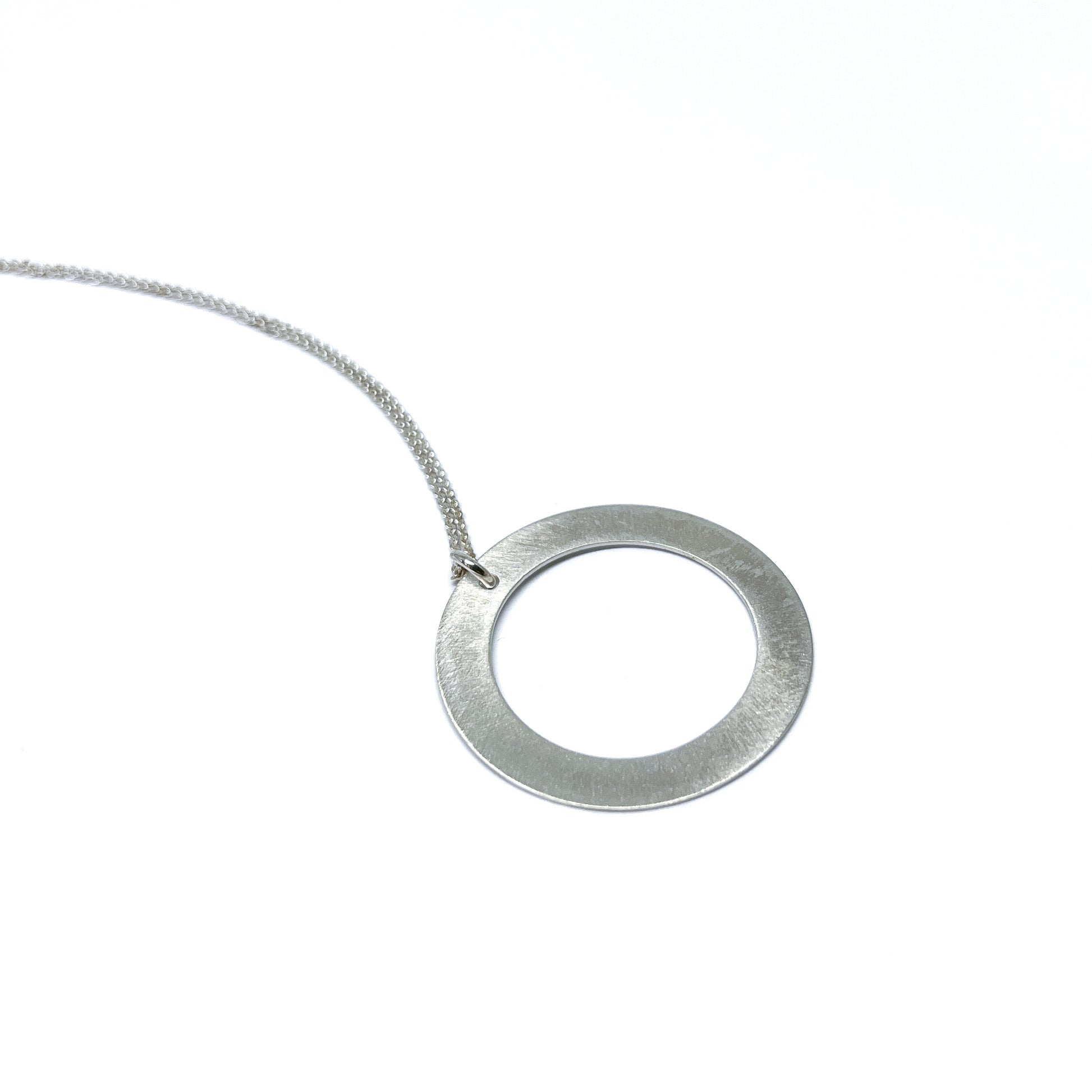 Silver necklace with a circular pendant, lying flat.