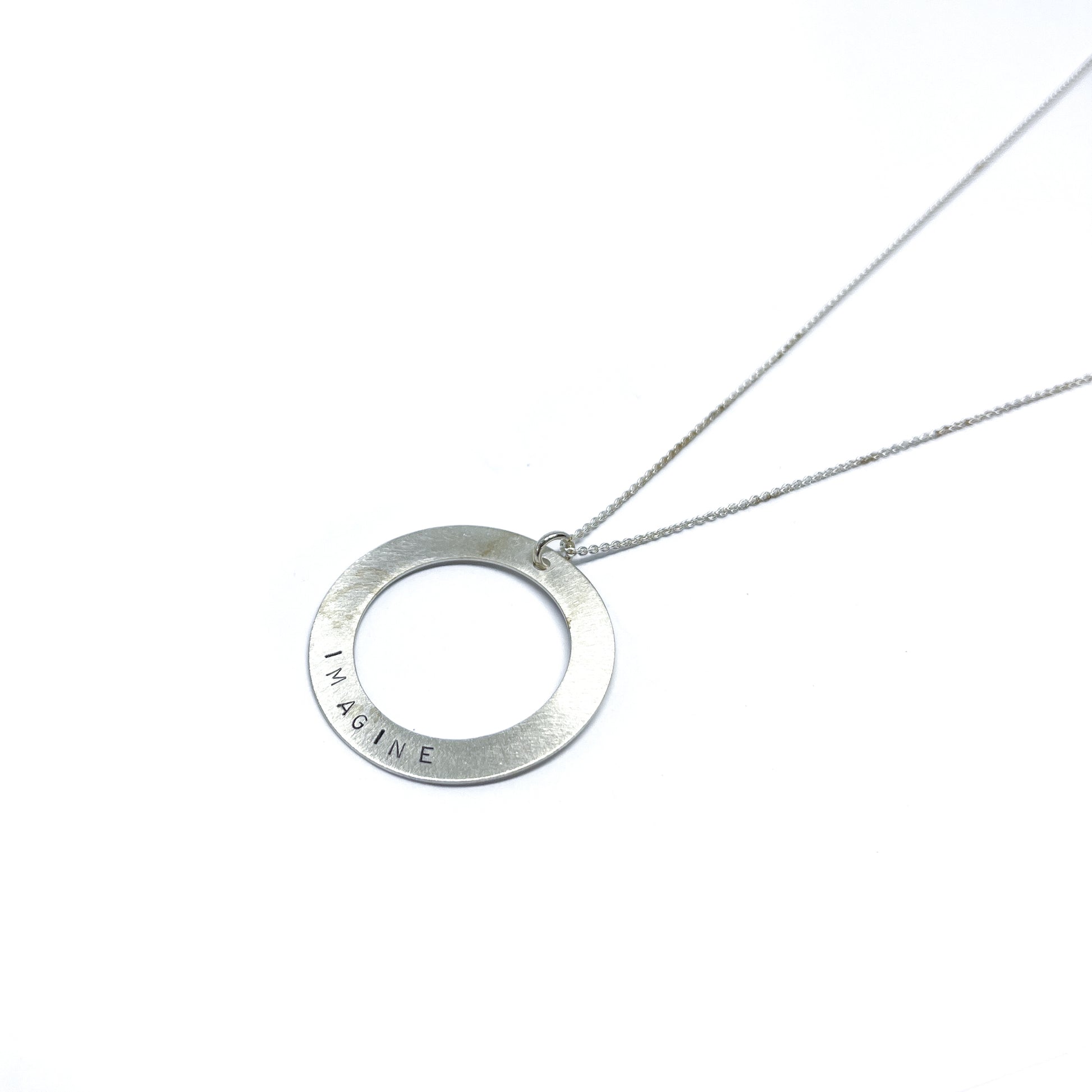 Silver necklace with a circular pendant engraved with the word "IMAGINE."