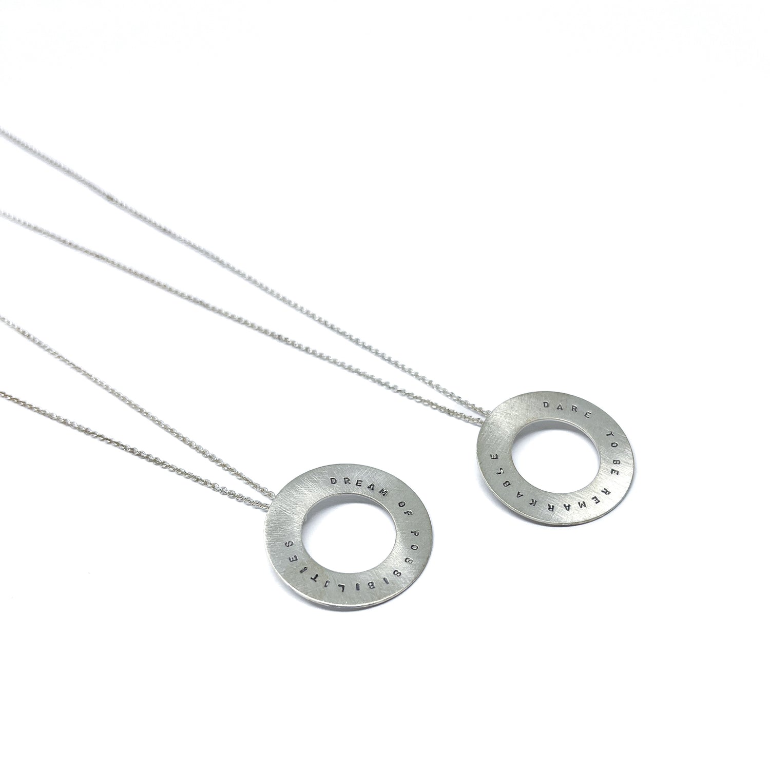 Two silver necklaces with circular pendants, each with inspirational words engraved around the edge.