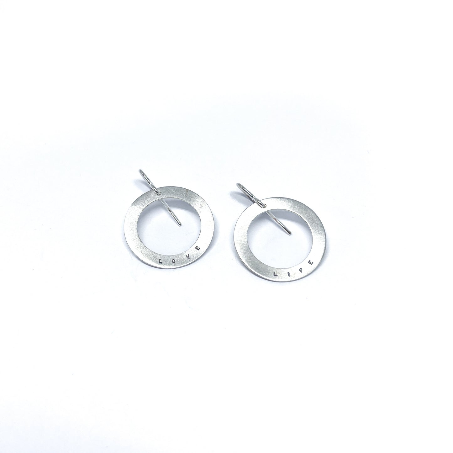 Two silver earrings with circular pendants, one engraved with "LOVE" and the other with "LIFE."
