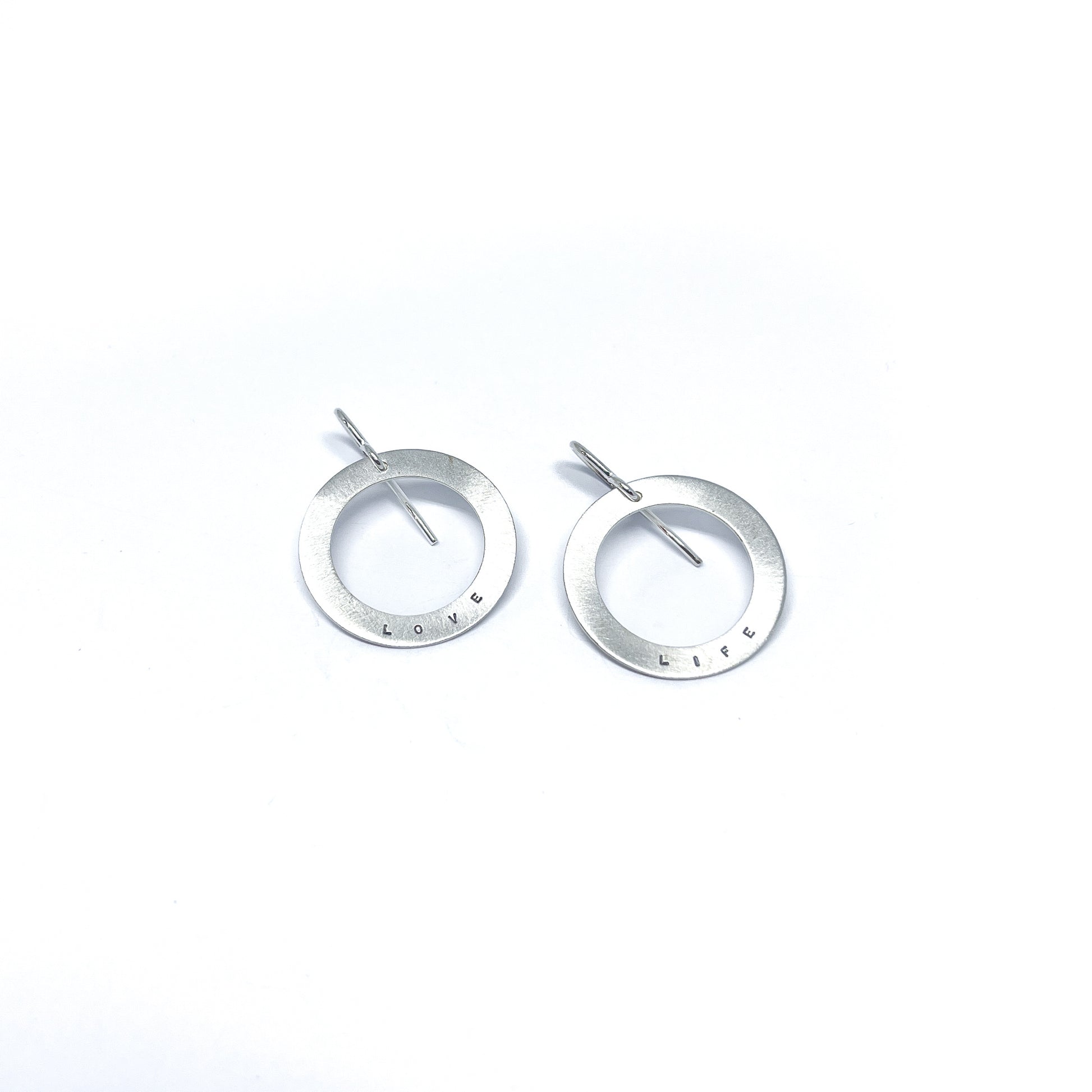Two silver earrings with circular pendants, one engraved with "LOVE" and the other with "LIFE."