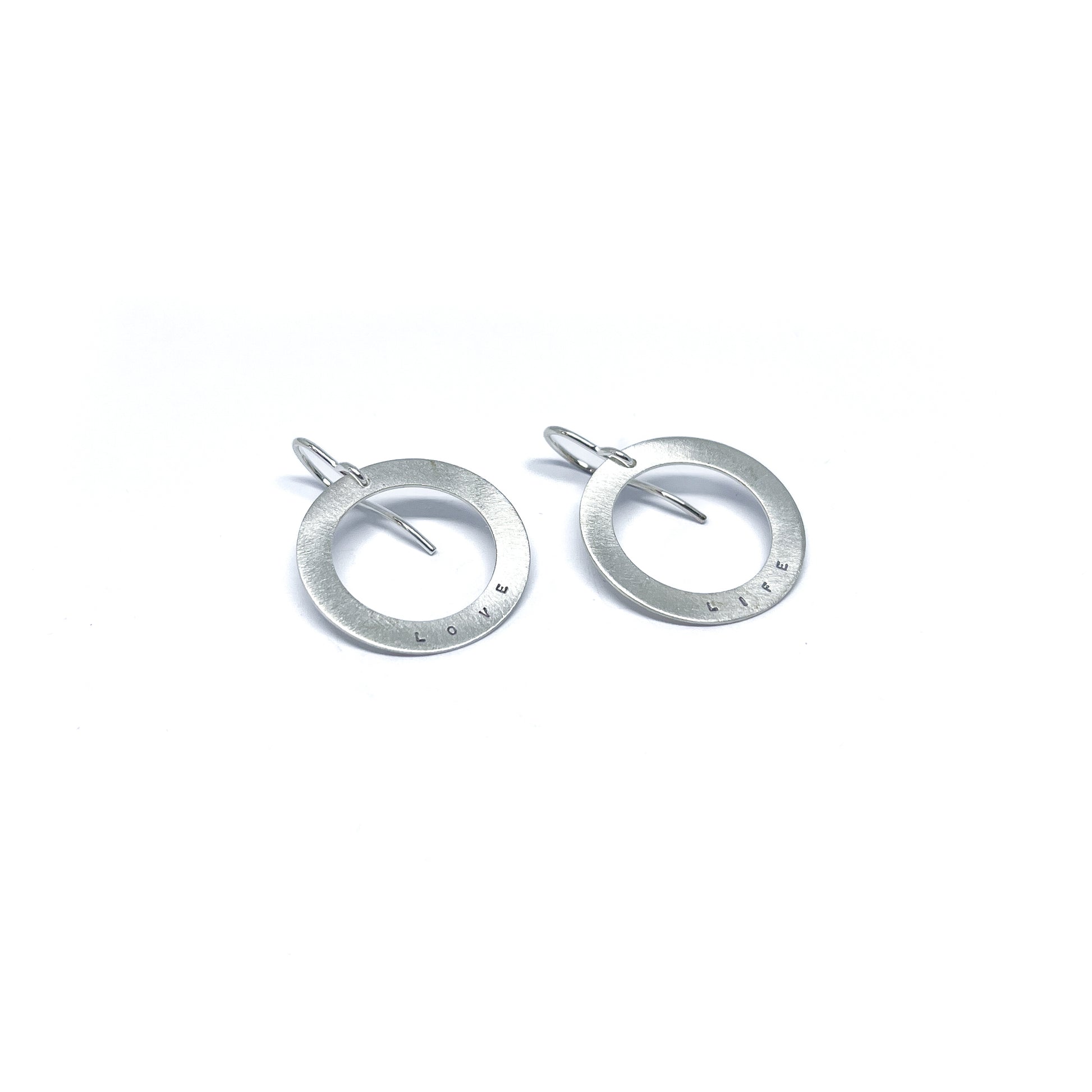 Two silver earrings with circular pendants, one engraved with "LOVE" and the other with "LIFE."