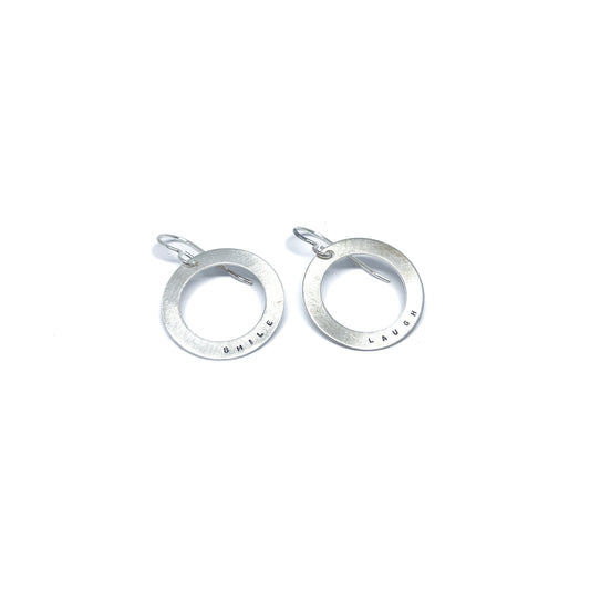 Two silver earrings with circular pendants, one engraved with "SMILE" and the other with "LAUGH."
