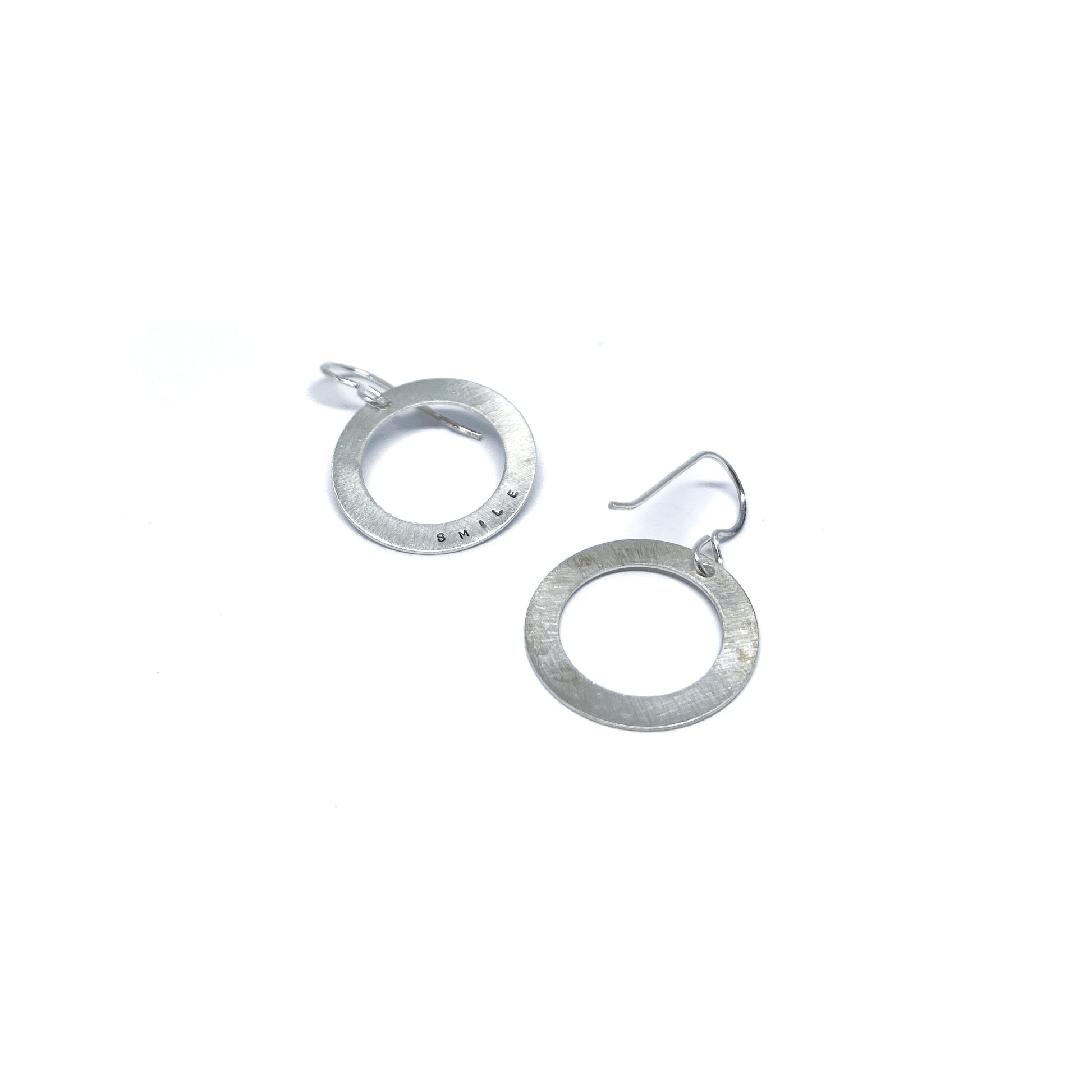 Two silver earrings with circular pendants, one engraved with "SMILE."
