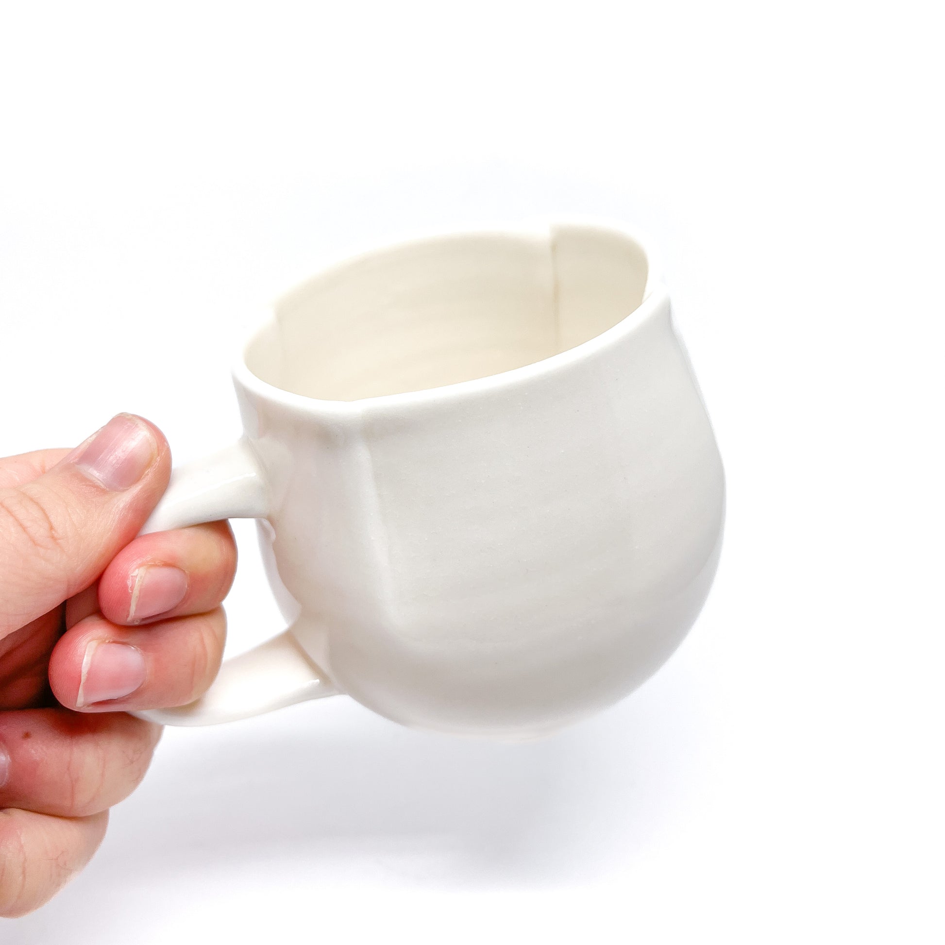 A hand holding a white ceramic mug with a handle, showing the smooth texture.