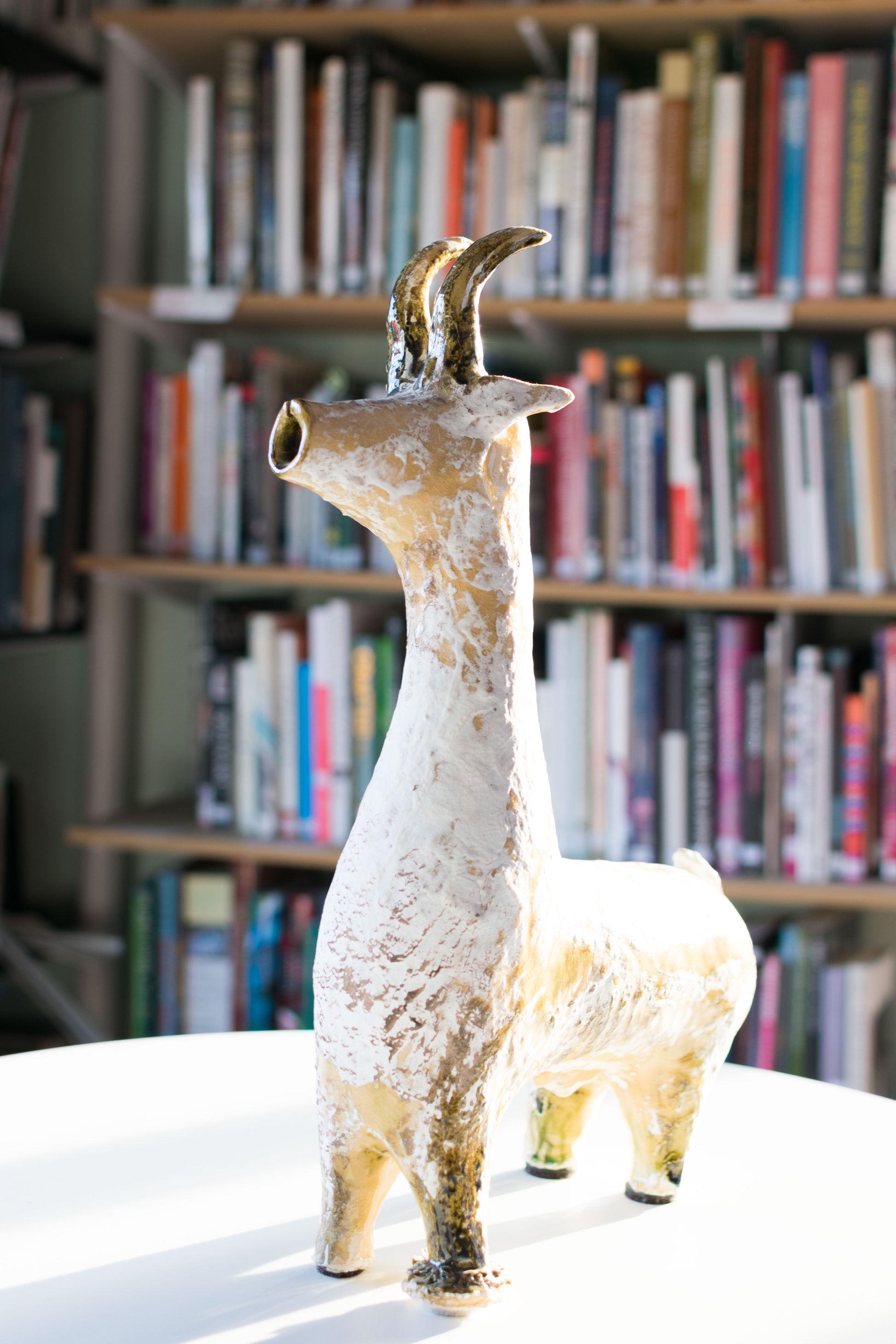 A textured ceramic Long Neck Bull sculpture with a long neck, curved horns, and a distressed light-toned glaze with white accents on a table.