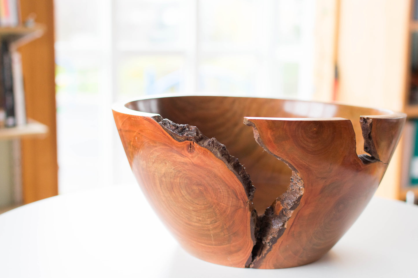 A wooden bowl with a natural crack, showing wood grain and a polished finish, sitting on a white surface.